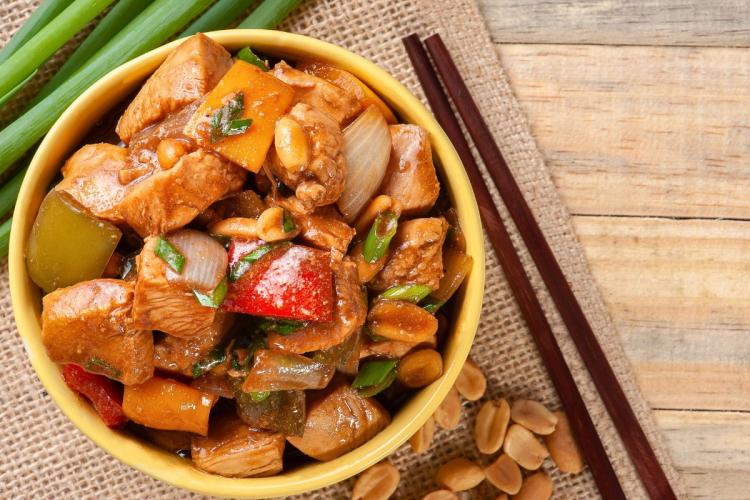 Un cuenco con pollo kung pao. Hay dos palillos al lado.