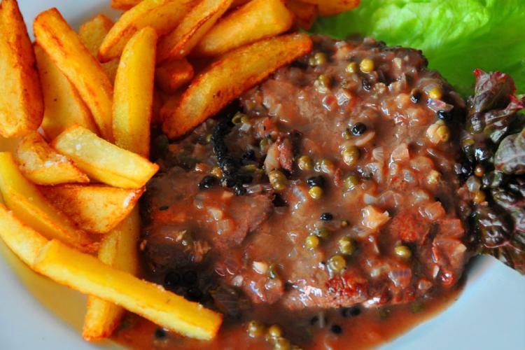 Un plato con un filete de cebú a la pimienta negra y verde acompañado de patatas fritas.