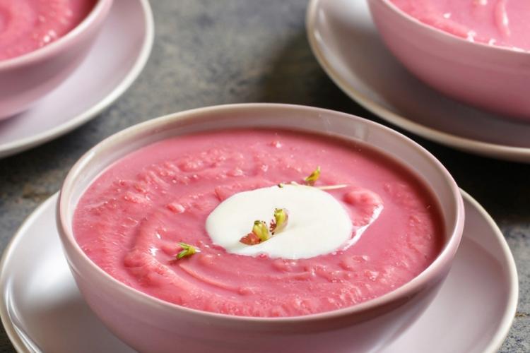 Un cuenco con sopa de terciopelo rosa decorada con crema de coco y pistacho picado.
