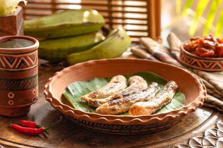 Boli sobre una hoja de banana dentro de un plato de barro y un recipiente con salsa picante al lado.