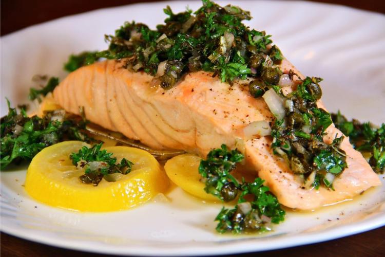 Salmón con vinagreta cítrica al perejil y alcaparras, acompañado de rodajas de limón.