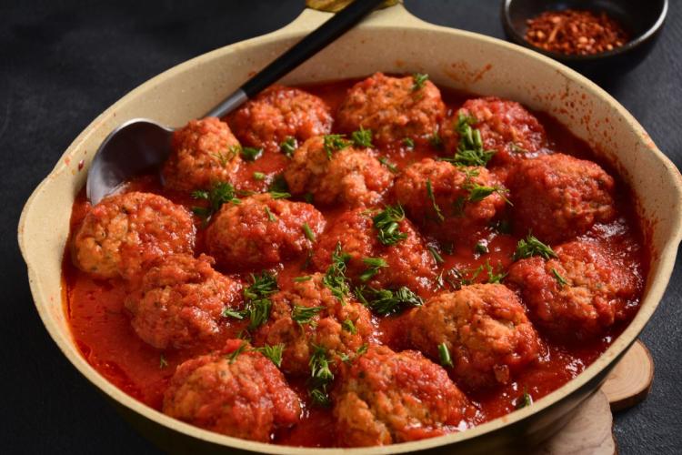 Una cazuela de cerámica con albóndigas de sepia y gambas en salsa de tomate.