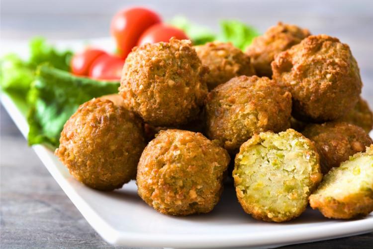 Un plato con varios falafel, uno de ellos cortado por la mitad y mostrando el interior.