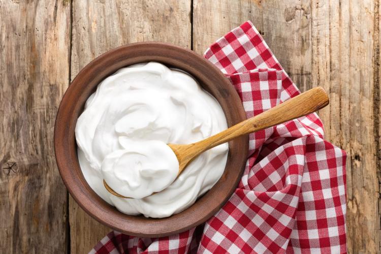 Un cuenco de madera con yogur natural con una cuchara de palo sobre una servilleta de cuadros en una mesa de madera.