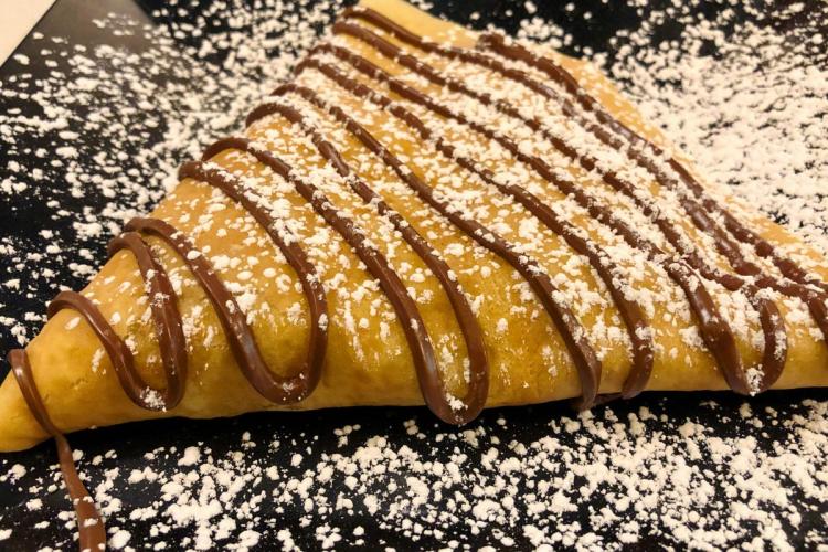 Crêpe doblada en forma de triángulo con salsa de chocolate y espolvoreada con azúcar glas.