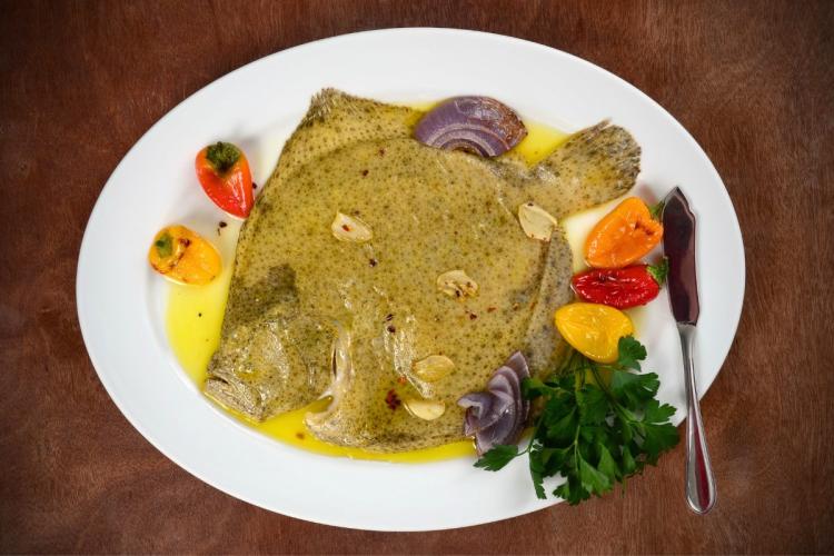 Un plato con un rodaballo escalfado cubierto de salsa gallega, acompañado de pimientitos.