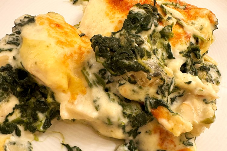 Una porción de filetes de merluza con besamel y espinacas en el plato.