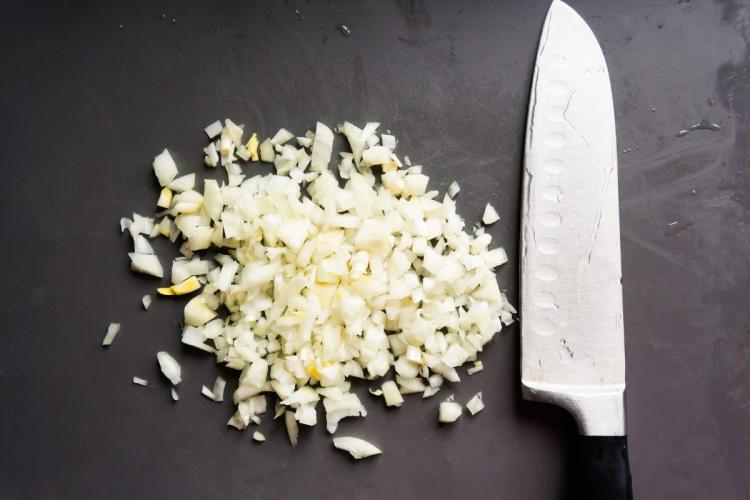 Cebolla picada sobre una tabla con un cuchillo afillado a su lado.
