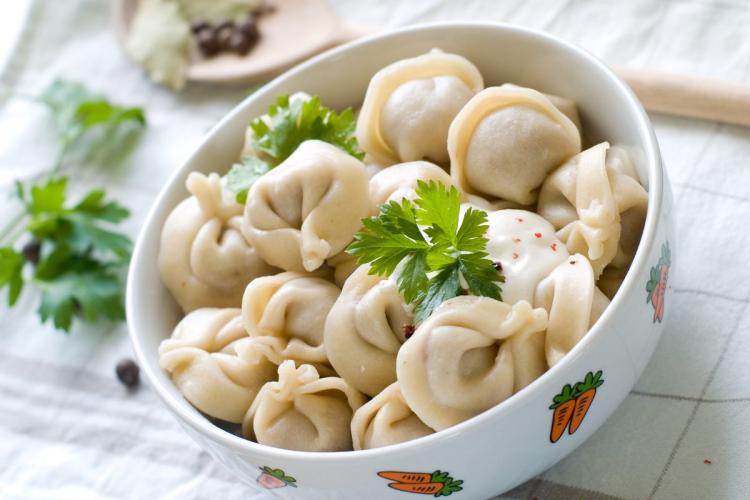 Un cuenco de pelmeni ruso con guarnición de eneldo fresco.