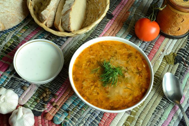 Un cuenco con shchi, una sopa tradicional rusa de col, adornada con eneldo fresco sobre un mantel de colores. 