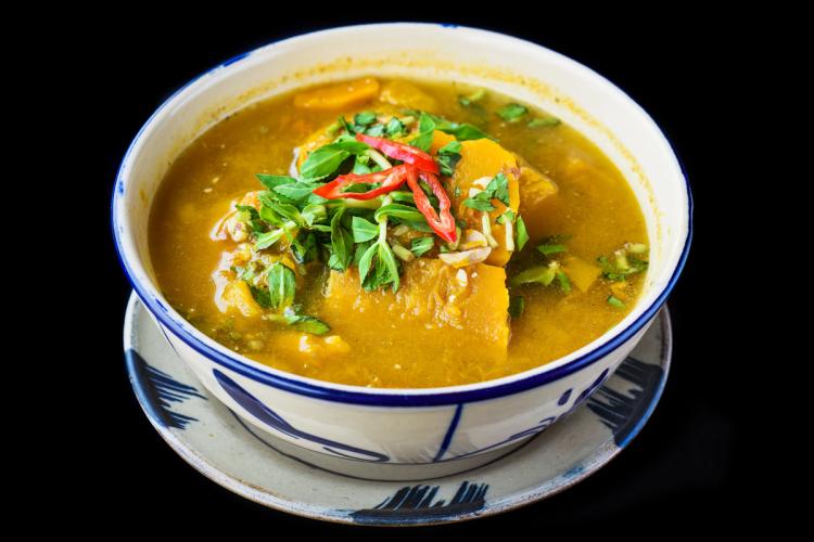Un cuenco con sopa vietnamita de calabaza contra un fondo negro.