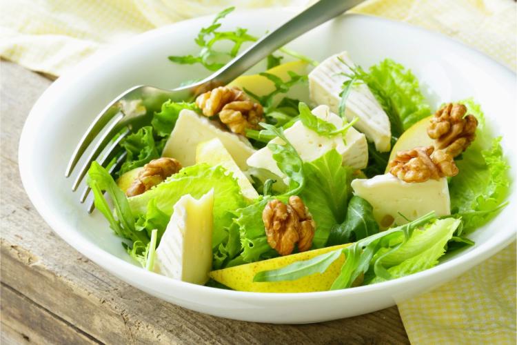 Un plato con ensalada de hojas verdes, queso camembert y pera.