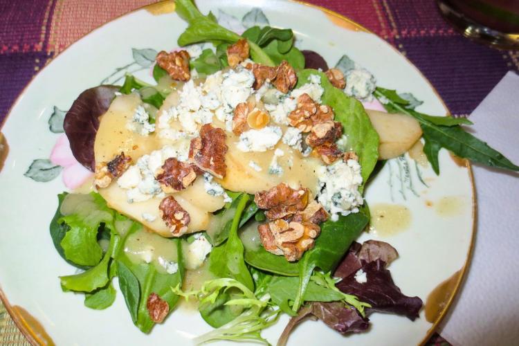 Un plato con ensalada de hojas variadas, queso azul, nueces y pera.