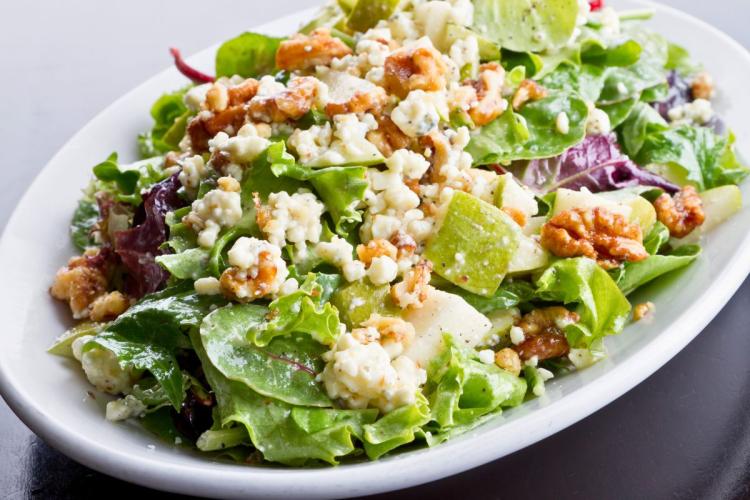 Un plato con ensalada de hojas variadas, requesón y manzana.