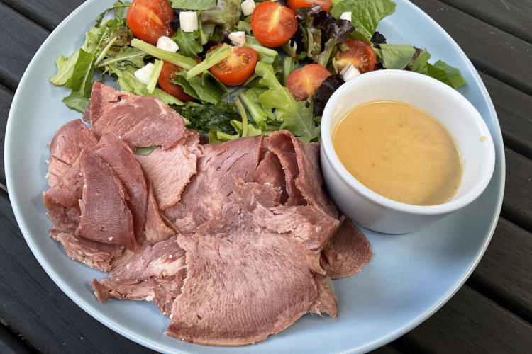 Lengua estofada con su salsa en un recipiente al lado, acompañada de una ensalada variada.