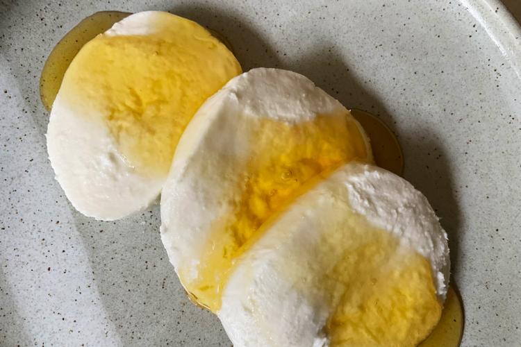Un plato con tres rodajas de queso mozzarella cubierto con melado.