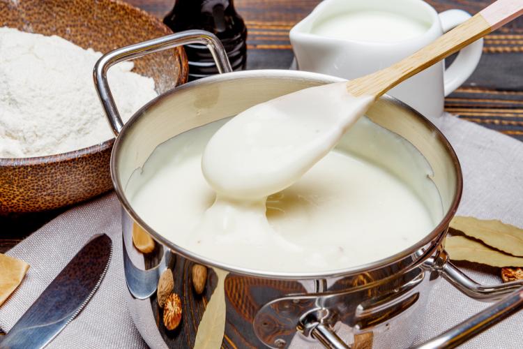 Un cazo con salsa bechamel con alguno de los ingredientes alrededor.