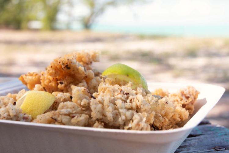 Fritos de caracol, cracked conch, con cuartos de lima en un contenedor rectangular