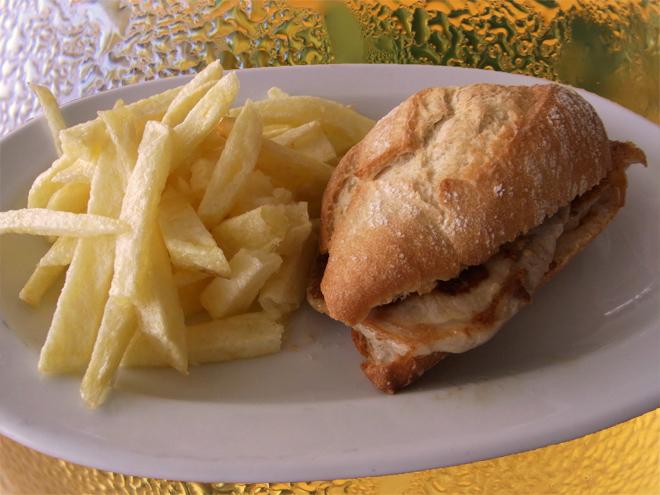 Montadito de lomo de cerdo y patatas fritas con jarras de cerveza al fondo.