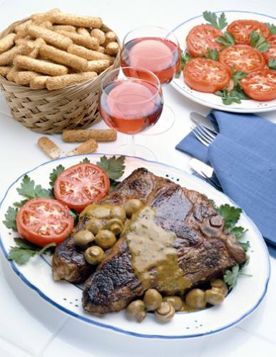Chuletones de buey con sus guarniciones acompañados de vino tinto.