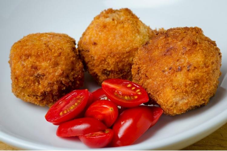 Croquetas de arroz y queso, arancini, recién hechas acompañadas de tomates miniatura.