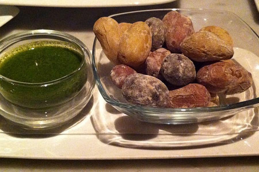 Papas arrugadas con un mojo verde en un cuenco al lado.