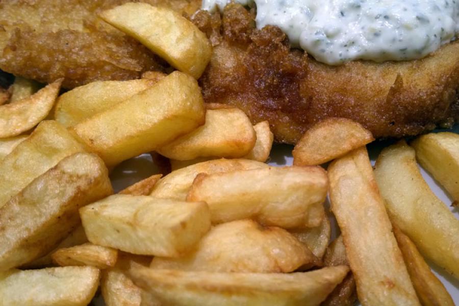 Un plato con pescado y patatas fritas, con salsa tártara.