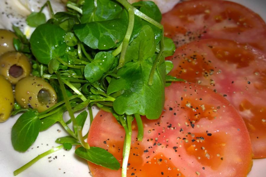Ensalada de rodajas de tomate, berros y aceitunas.