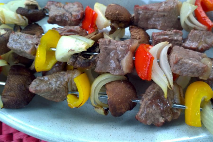 Ters pinchos de carne, piiento, cebolla, y champiñones en una fuente.