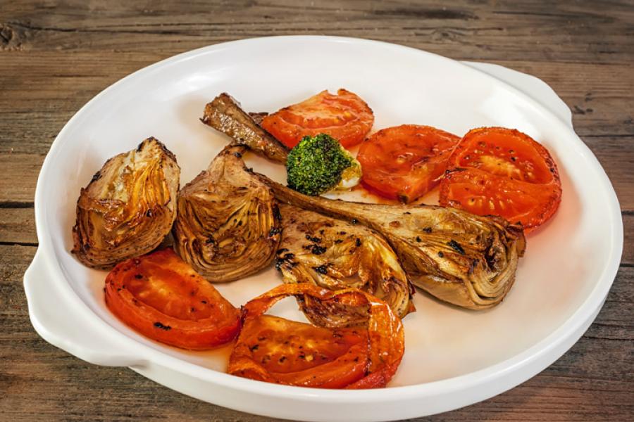 Alcachofas y tomate asados en un plato.