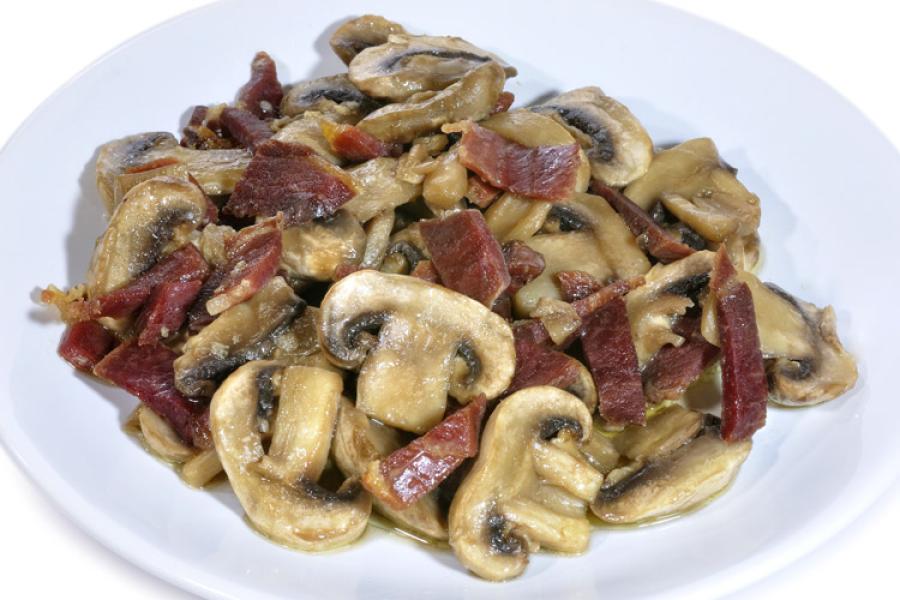 Champiñones salteados con jamón serrano en plato blanco.