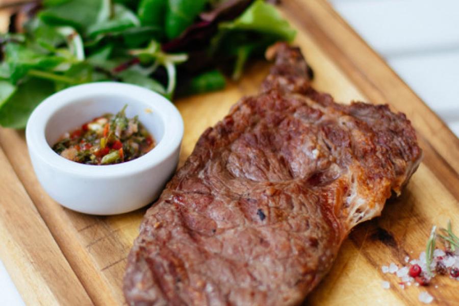 Filete a la plancha sobre tabla de madera acompañado de  salsa y canónigos.