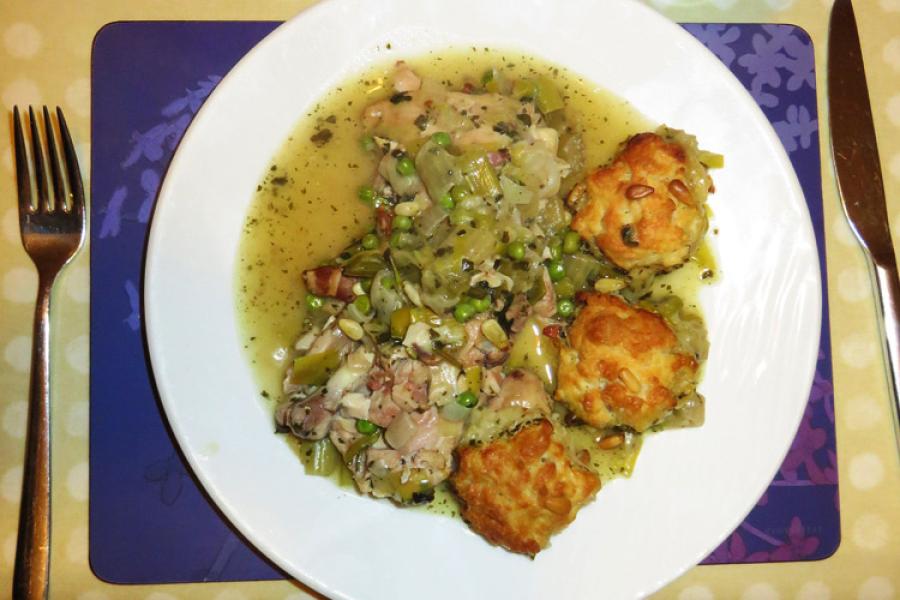 Una ración de cazuela de pollo al pesto con bolas de queso y piñones servida en plato.