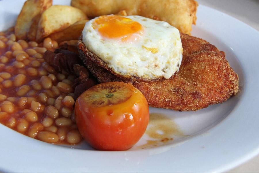 Plato de pollo empanado con un huevo a caballo, alubias al horno y patatas fritas.