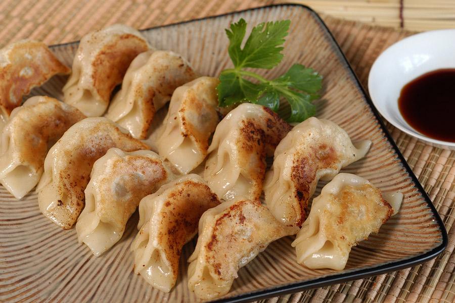 Una fuente con gyoza ya cocinado y un cuenco con salsa para mojar al lado.