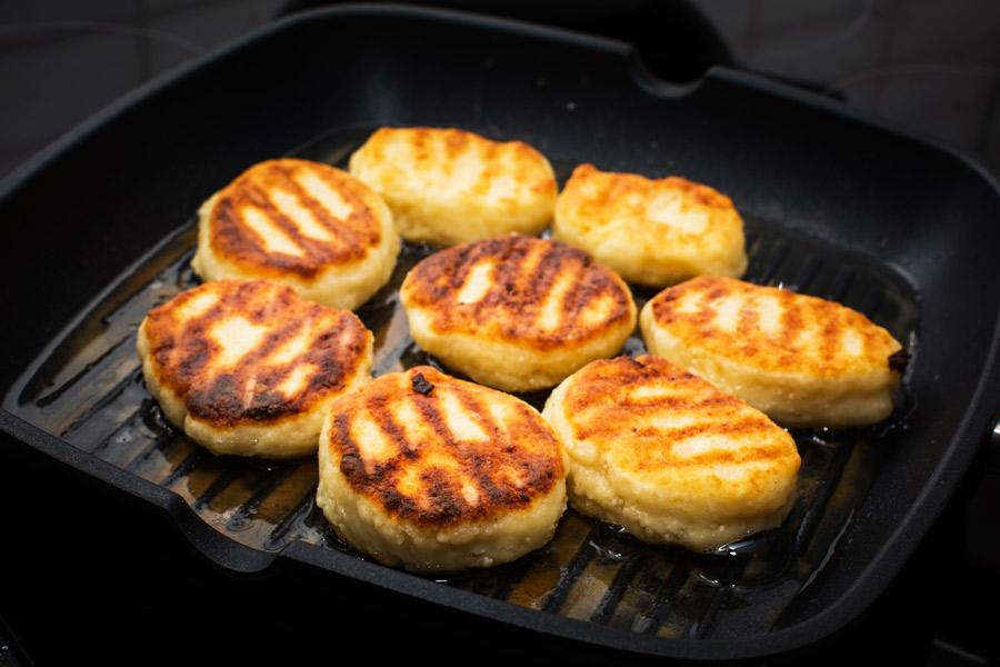 Syrniki, tortitas de queso fresco y blando fritas, en una sartén.