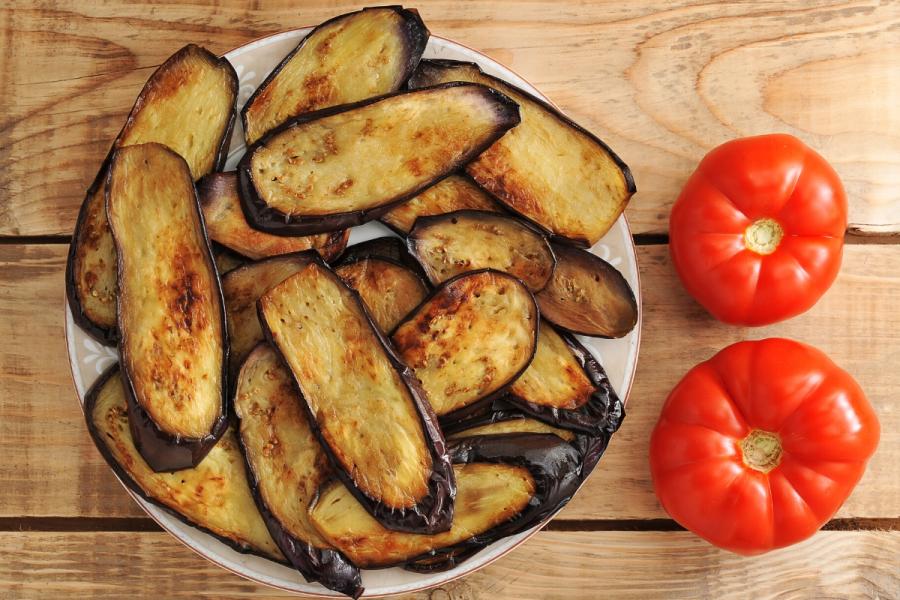 Berenjenas fritas en un plato junto a dos tomates.