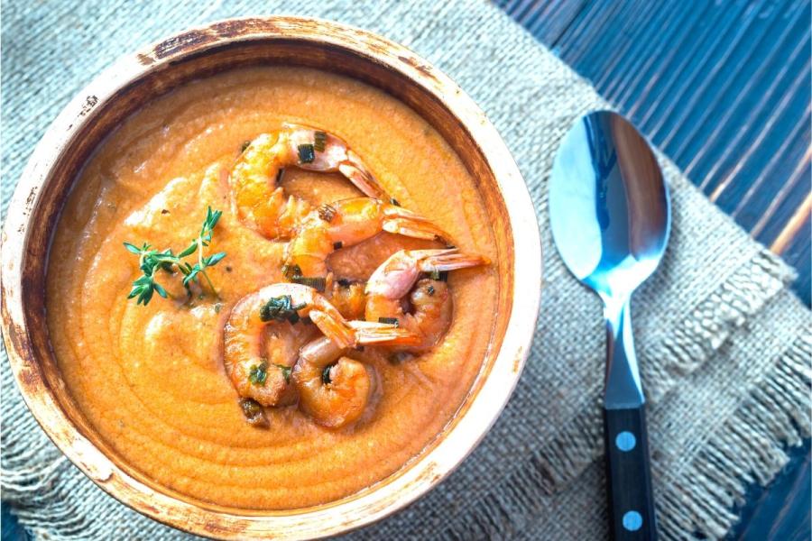 Crema de langostinos en un cuenco, decorada con colas de langostinos y hierbas.