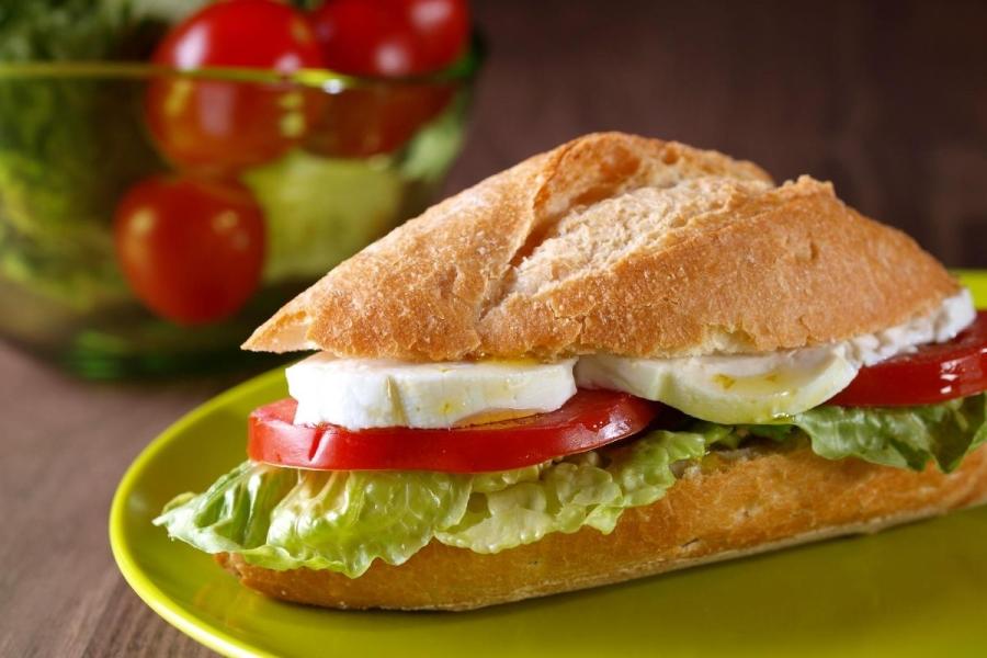 Bocadillo de queso de cabra, tomate y lechuga en barra de pan.