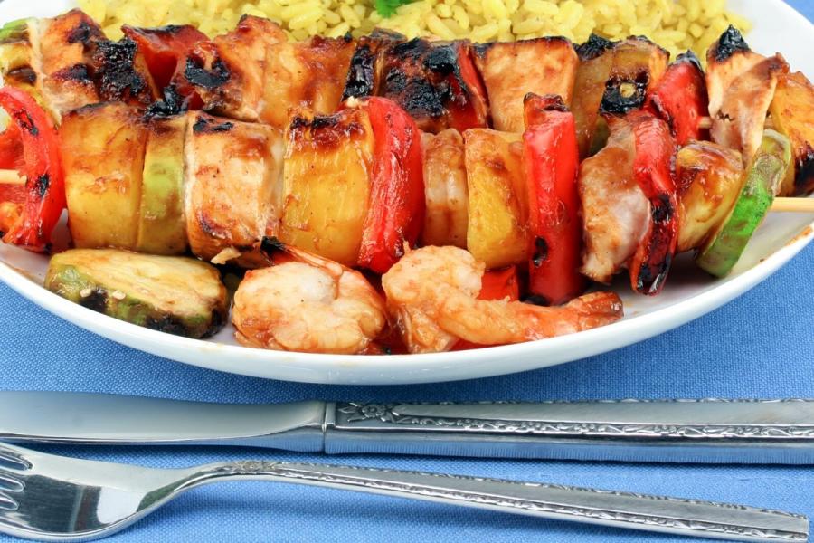 BRochetas de pollo y piña con su acompañamiento en un plato.