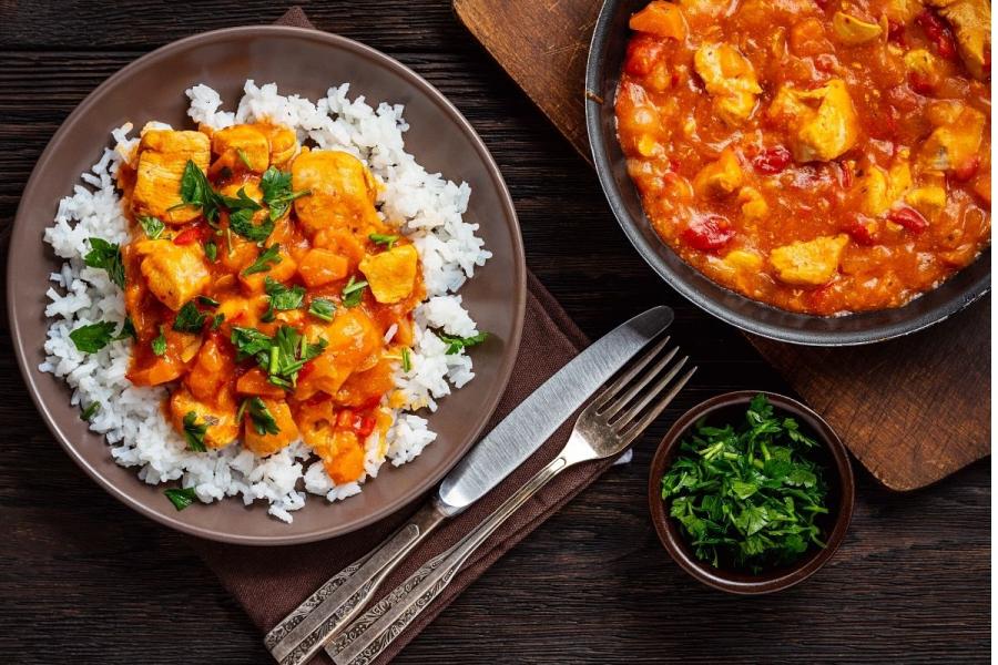 Goulash de pollo con arroz blanco, decorado con perejil picado.