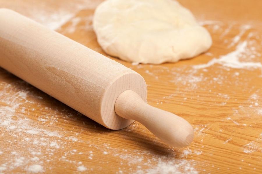 Masa lista para estirar sobre superficie enharinada y un rodillo de madera.