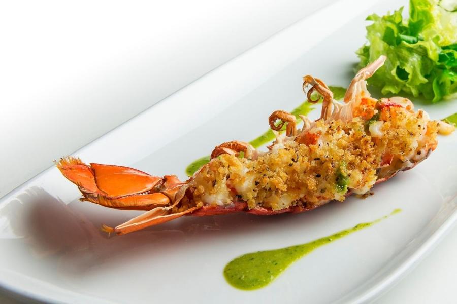 Cola de langosta gratinada en una fuente acompañada de ensalada.