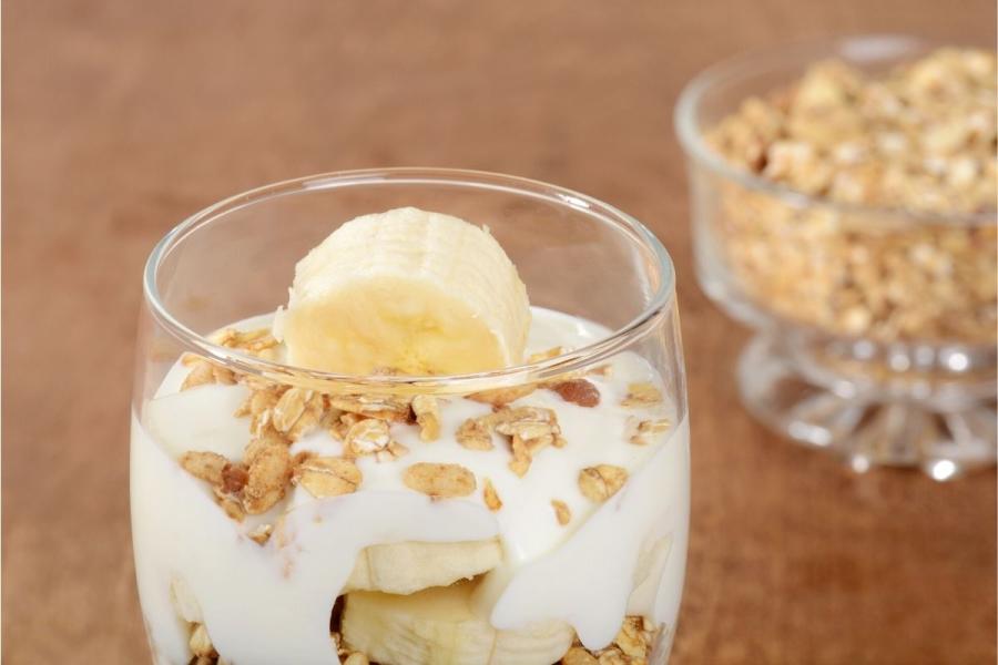 Copa de plátano, yogur y granola en vaso de globo.
