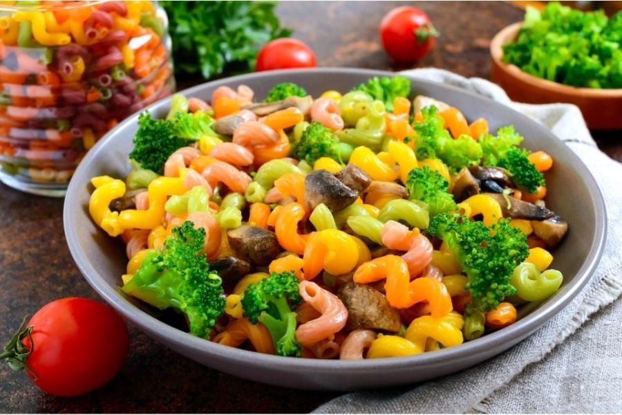 Un plato de loza lleno de pasta tricolor con brócoli y champiñones.