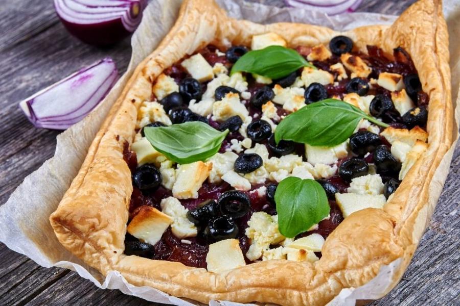 Tarta de cebolla morada y queso feta decorada con aceitunas negras y albahaca fresca.