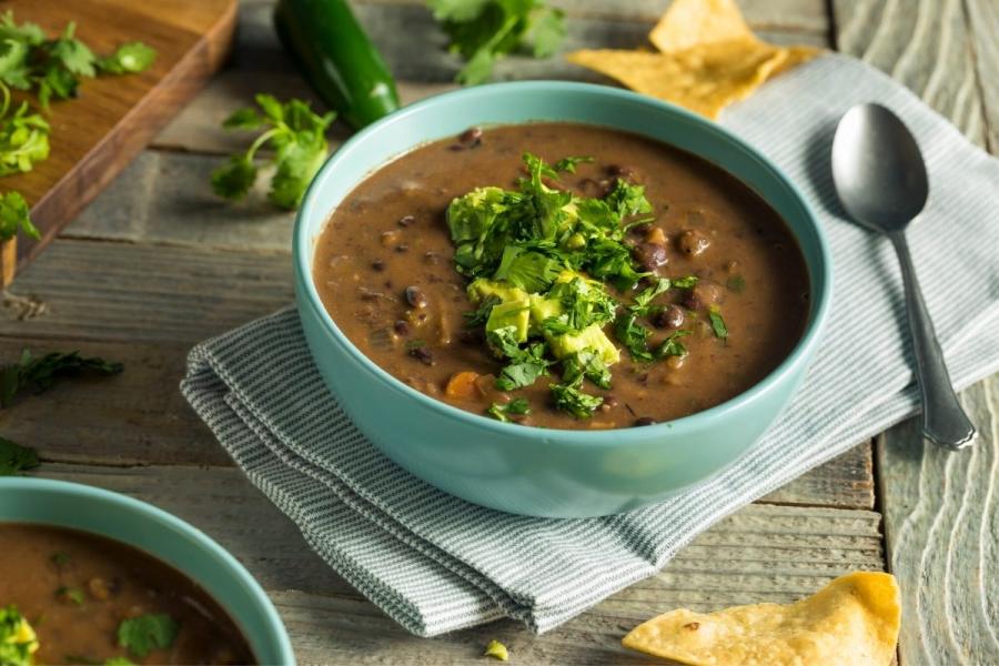 Sopa de frijoles negros adornada con aguacate y cilantro.