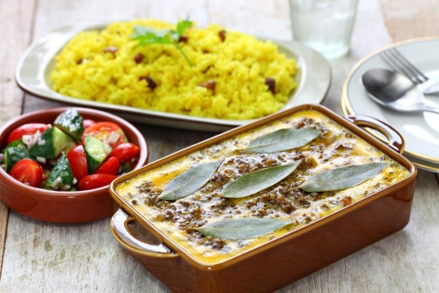 Una fuente con bobotie recién hecho acompañada un cuenco de sambal y una fuente de arroz pilau.
