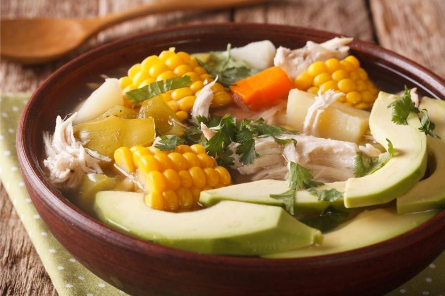 Un cuenco de ajiaco con zanahoria añadida y guarnición de cilantro fresco y aguacate.
