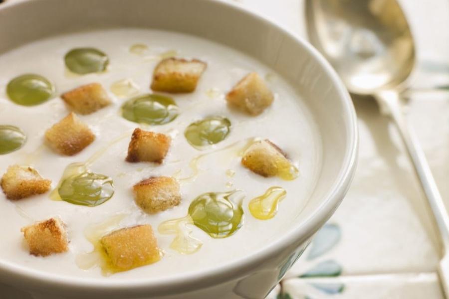 Plato de ajo blanco malagueño con guarnición de pan frito y uvas.